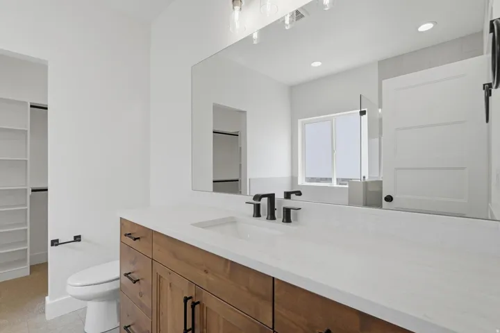 Bathroom vanity featuring a wood-finish cabinet, white countertop, and matte black fixtures