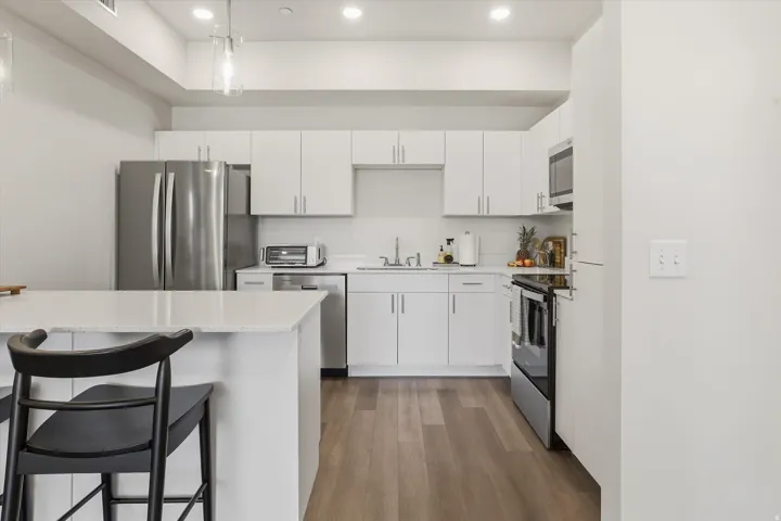 Modern kitchen featuring a white quartz-finish island, stainless steel appliances, white cabinetry, recessed lighting, and wood-finish flooring