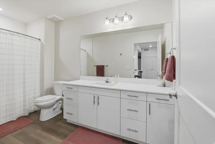 Bathroom featuring a white vanity with extensive counter space and storage, a large wall-mounted mirror, brushed nickel hardware, and wood-finish flooring