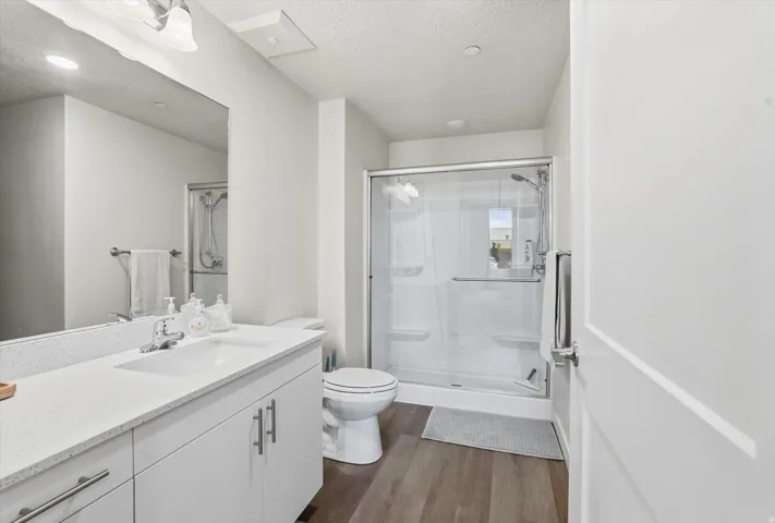 Full bathroom featuring a white vanity with a quartz-finish countertop and undermount sink, a large mirror, a glass-enclosed shower with a built-in bench, and wood-finish flooring