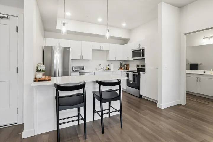 Modern kitchen featuring white cabinetry, stainless steel appliances, a white countertop island with seating, and wood-finish flooring