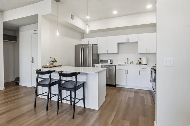Modern kitchen featuring a central island with countertop seating, white cabinetry, integrated stainless steel appliances, and wood-finish flooring