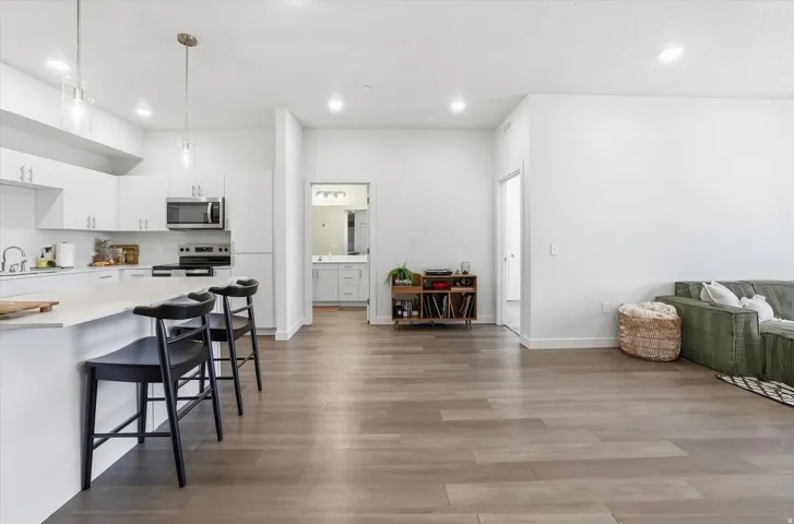 Open-concept kitchen and living area featuring wood-finish flooring, white cabinetry, stainless steel appliances, and a kitchen island with seating
