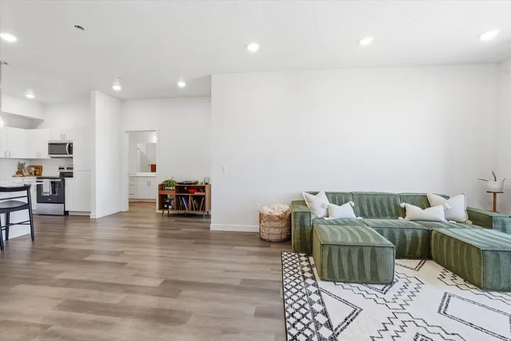 Open-concept living area featuring wood-finish flooring, recessed lighting, and a kitchen with white cabinetry and stainless steel appliances