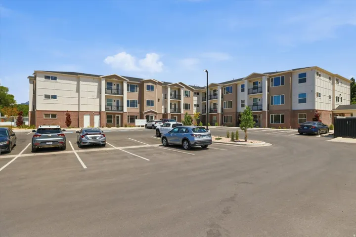 Contemporary multi-story building featuring brick and siding accents, multiple private balconies, and a paved parking area with designated spaces