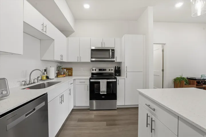 Modern kitchen featuring white cabinetry, light-toned countertops, stainless steel appliances, and wood-finish flooring
