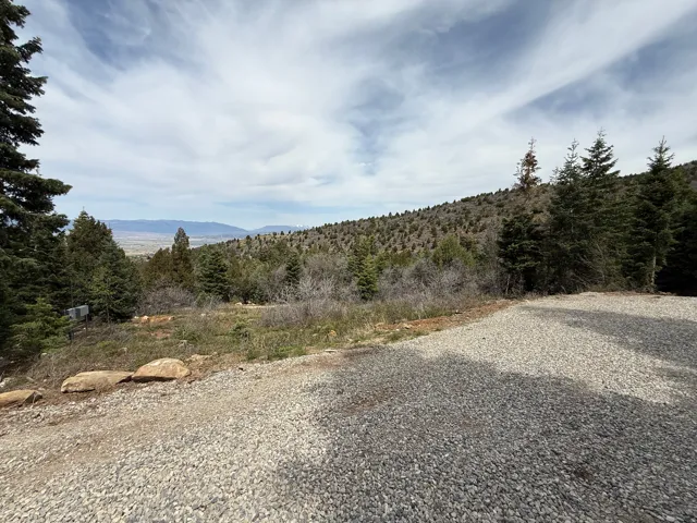 Gravel surface with surrounding natural landscape, including prominent evergreen trees and distant hills