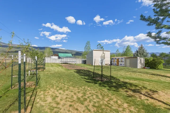 Large fenced perimeter, mountain backdrop, mature trees, and storage sheds.