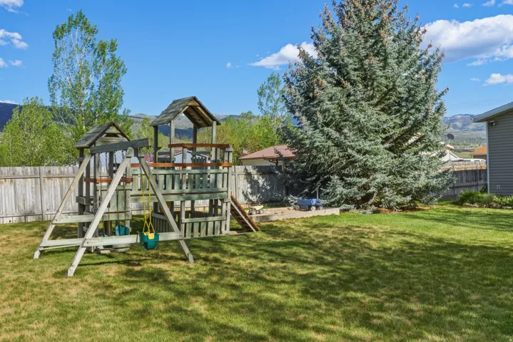 Expansive backyard featuring a lush lawn, a mature evergreen tree, and a wooden play structure with multiple levels and swings