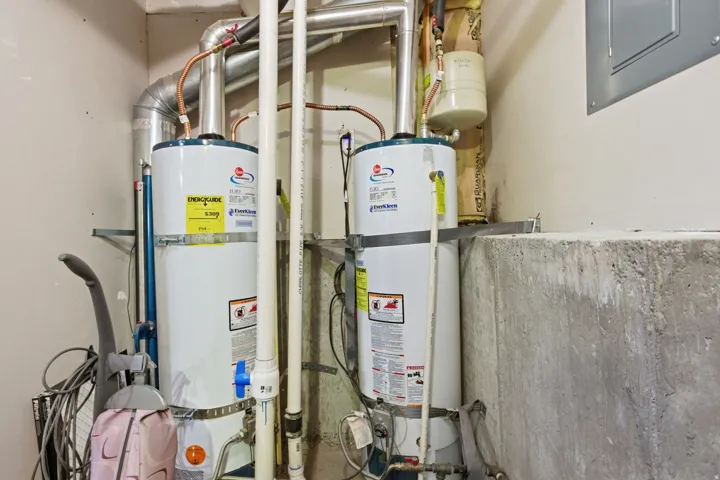 Dual water heaters with overhead ventilation piping and exposed utility lines, set against a concrete foundation wall