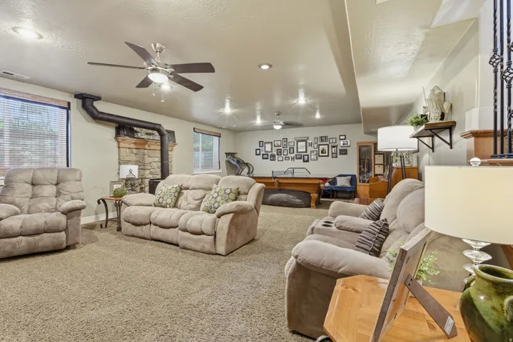 Carpeted recreation room featuring a stone-clad fireplace with wood-burning stove, recessed lighting, and dual ceiling fans