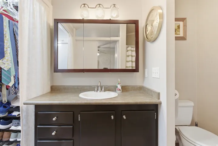 Vanity area featuring a single basin sink, laminate countertop, dark wood-finish cabinetry with silver hardware, and a framed medicine cabinet with overhead lighting