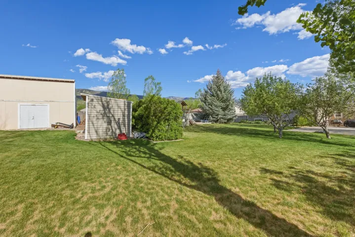 Expansive green lawn with mature trees and a large detached storage building featuring double doors