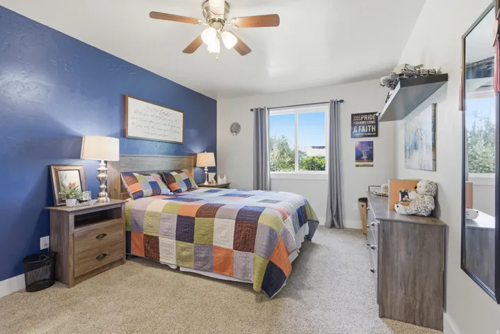 Carpeted room featuring a ceiling fan with light fixture, a window with curtains, and a wood-finish headboard