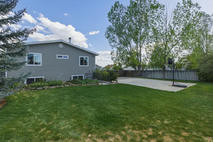 Expansive backyard featuring a concrete sport court, mature trees, manicured lawn, and a privacy fence