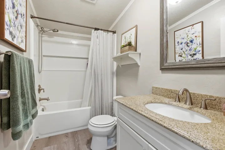 Bathroom featuring a white bathtub with shower, light wood-finish flooring, a white vanity with a light speckled countertop, and a framed mirror