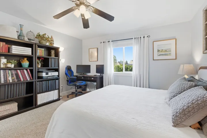 Neutral-toned bedroom featuring carpet flooring, a ceiling fan with integrated lighting, and a large window with white curtains
