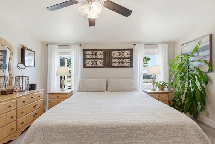 Bedroom featuring two windows with white curtains, a ceiling fan with light fixture, and light wood-finish flooring
