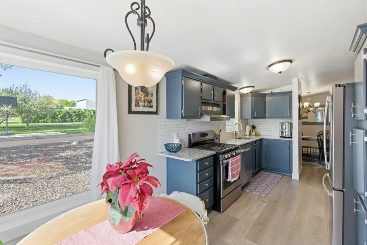 Kitchen featuring blue cabinetry, granite-style countertops, stainless steel appliances, subway tile backsplash, and wood-finish flooring