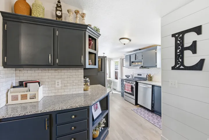 Kitchen featuring dark cabinetry, light-toned wood-finish flooring, stainless steel appliances, a white subway tile backsplash, and light-toned countertops