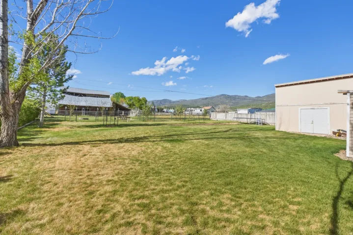 Expansive grassy yard with mountain backdrop and a large storage shed featuring a double door entry