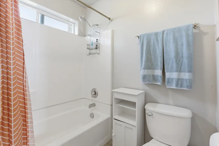 Bathtub and shower combination featuring a window, white surround, and chrome fixtures