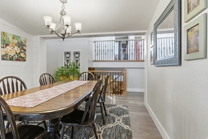 Spacious dining area featuring wood-finish flooring, a contemporary chandelier, and shiplap accent wall