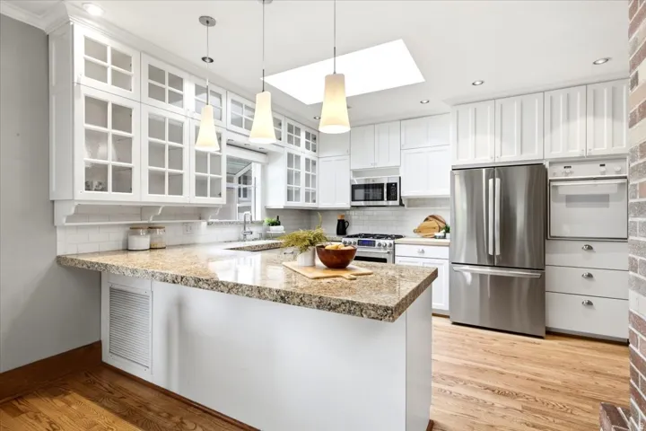 Kitchen featuring a skylight, white shaker-style cabinetry, granite countertops, stainless steel appliances, and wood-finish flooring