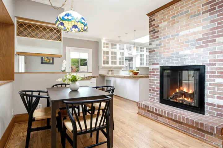 Hardwood-style flooring, brick fireplace with hearth, built-in wine rack, kitchen featuring white cabinetry, and granite countertops