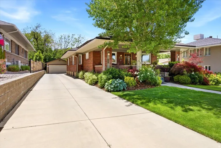 Brick exterior home featuring a well-maintained lawn, mature trees, and extensive landscaping