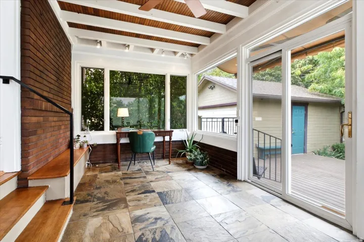 Exposed brick wall with built-in bench seating, wood-finish stairs with metal railing, floor-to-ceiling windows, wood-paneled ceiling with exposed beams, and stone tile flooring