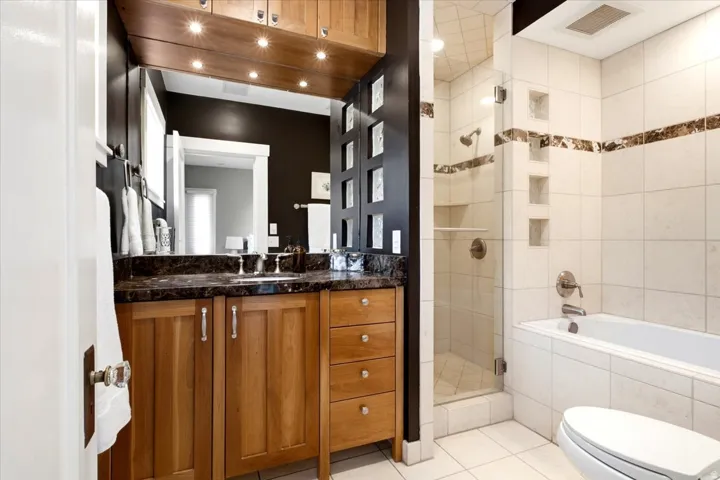 Wood-finish vanity with a dark countertop and integrated sink, accompanied by a tub and separate shower with glass enclosure