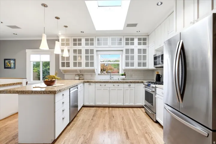 Kitchen featuring a skylight, wood-finish flooring, white cabinetry, stainless steel appliances, and a U-shaped countertop