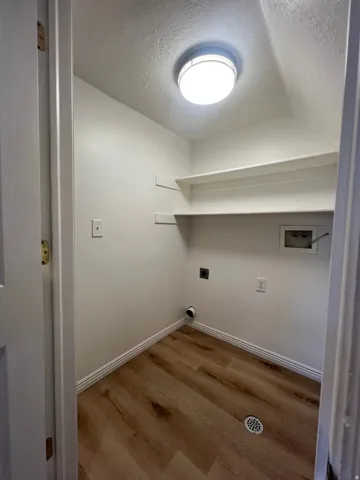 Dedicated laundry room featuring wood like flooring, bright lighting, open shelving for convenient access and organization