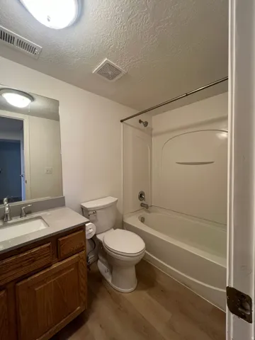 Full bathroom featuring a single vanity with wood-finish cabinetry, a white rectangular sink, new toilet and full tub/shower