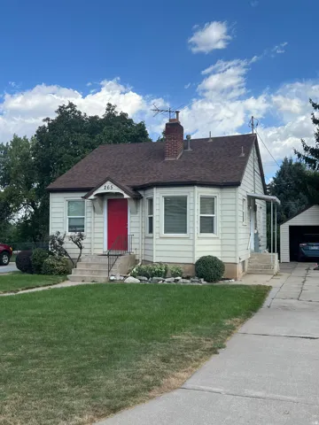 Cottage-style home featuring a red front door, light-colored siding, and a gabled roof