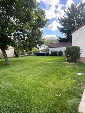 Expansive grassy yard with mature trees and a detached garage featuring a shingle roof