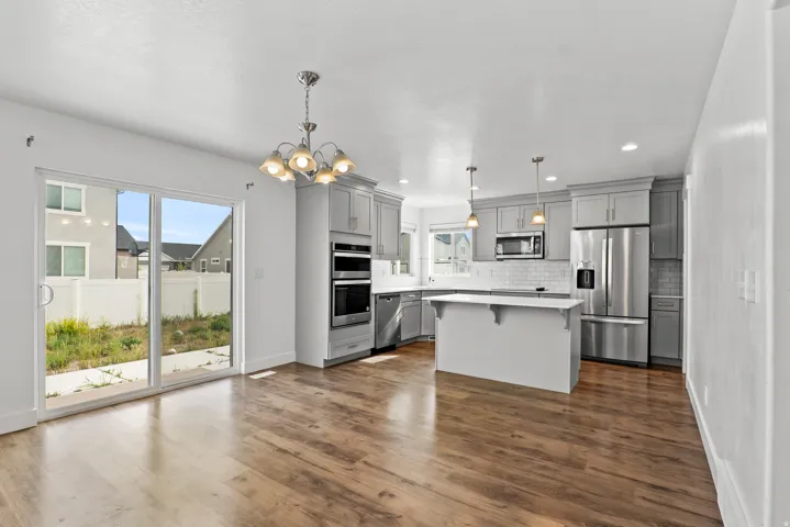 Open-concept kitchen and dining area featuring wood-finish flooring, gray cabinetry, stainless steel appliances, a center island, and sliding glass doors to the backyard