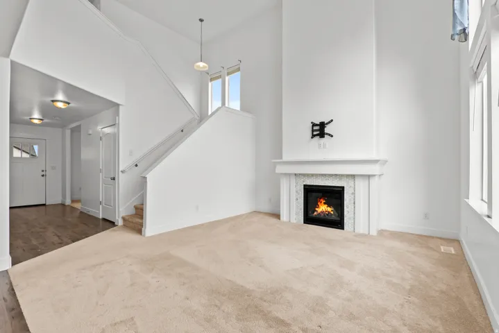 Living space featuring a gas fireplace with a tiled surround and mantel, high ceilings, large windows, wood-finish flooring at the entry, and carpeted stairs with a white railing