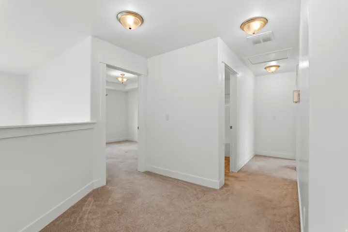 Carpeted hallway featuring bright white walls, ceiling-mounted dome light fixtures, and white trim