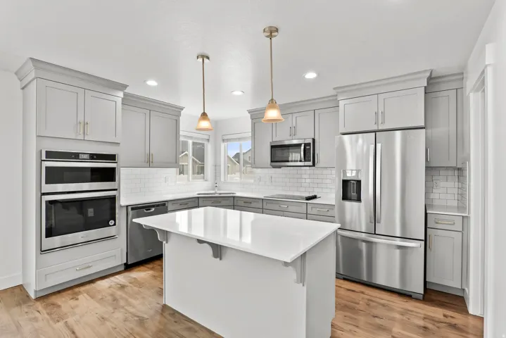 Kitchen featuring an expansive center island with a white countertop, full suite of stainless steel appliances, light gray cabinetry, subway tile backsplash, and wood-finish flooring