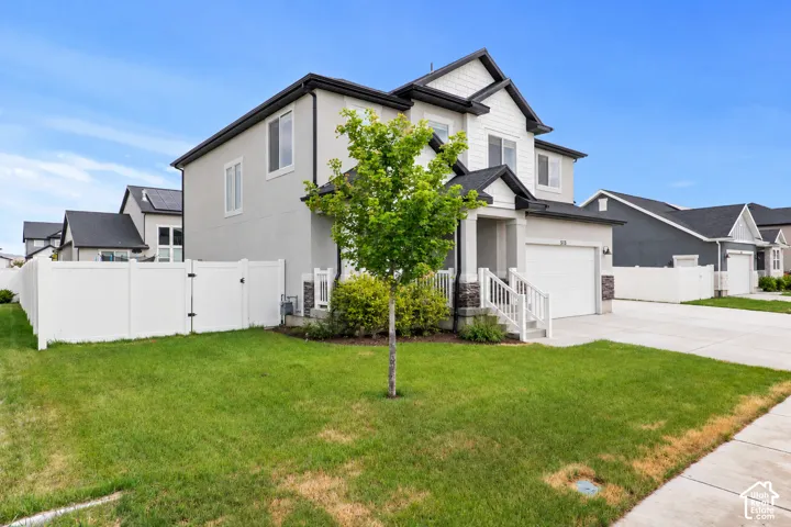 Two-story exterior featuring a mix of stucco and shaker-style siding, stone veneer accents, a gabled roofline, a two-car garage, and white vinyl perimeter fencing
