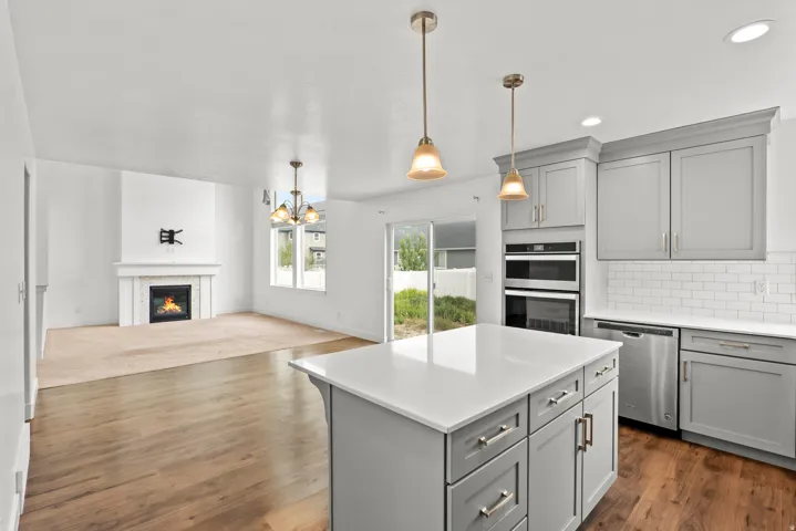 Modern kitchen featuring a large island with a light-toned countertop, pendant lighting, shaker-style cabinetry, and stainless steel appliances
