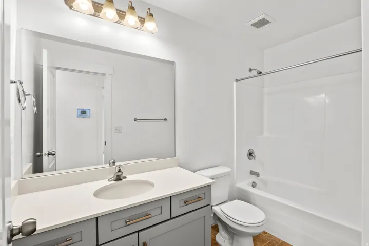 Bathroom featuring a light gray vanity with a white countertop and undermount sink, a large wall-mounted mirror, a four-light fixture, a white toilet, and a white tub/shower combination