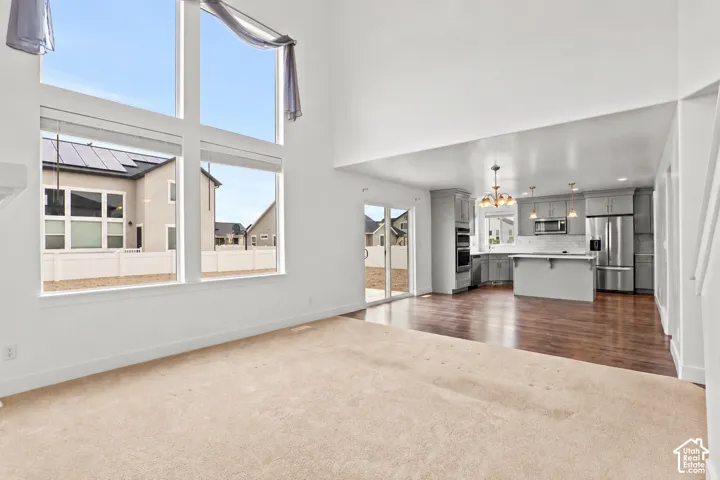 High-ceilinged living area featuring oversized windows, wood-finish flooring, kitchen island, built-in stainless steel double wall ovens, and glass door access to the rear exterior
