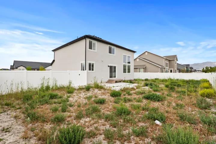 Rear exterior of a two-story residence with light-colored stucco siding and a dark roof