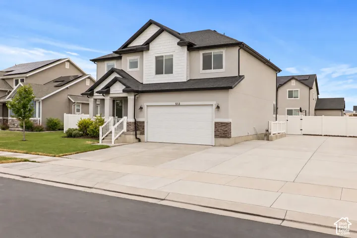 Two-story residence featuring a combination of stucco and shingle siding, stacked-stone accents, an attached two-car garage, and a white vinyl privacy fence