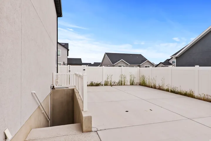 Concrete patio with a privacy fence, exterior stucco siding, and a basement access stairwell with handrails