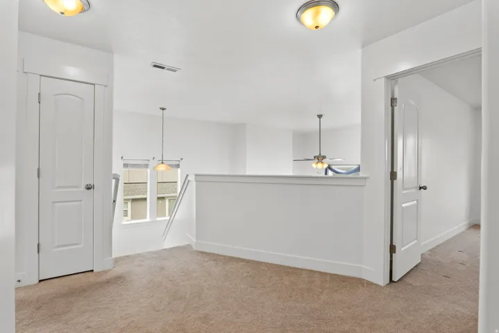 Carpeted landing featuring a white railing, two paneled doors, and ceiling-mounted light fixtures