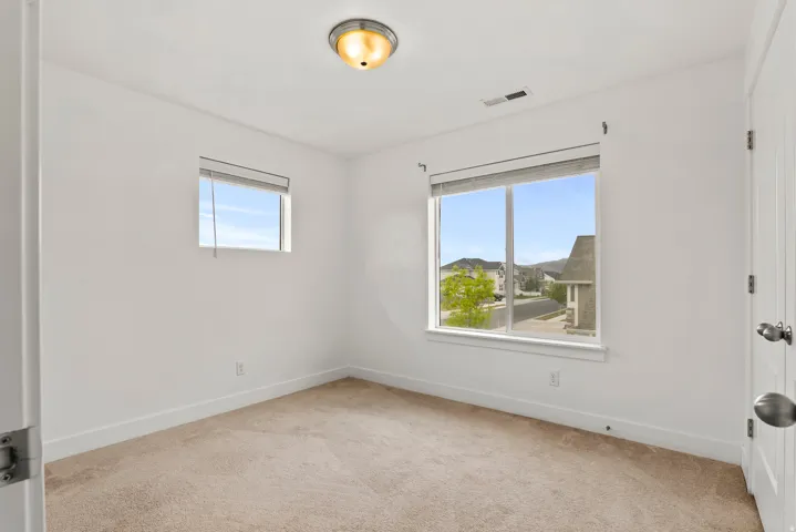 Bright room featuring two windows, neutral wall tones, plush carpeting, a flush-mount ceiling light fixture, and white trim